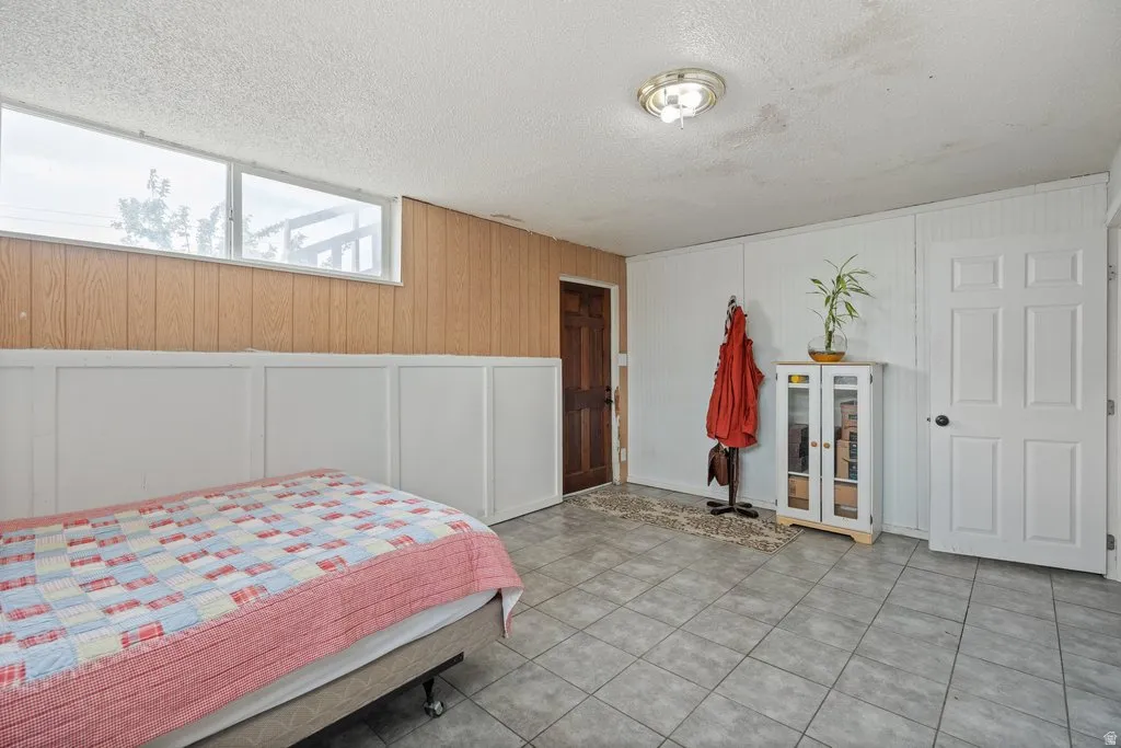 Bedroom featuring a decorative wall, wooden walls, a textured ceiling, and light tile patterned flooring