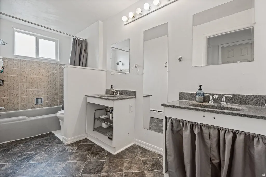 Bathroom featuring two vanities, a baseboard radiator, and shower / bath combo with shower curtain