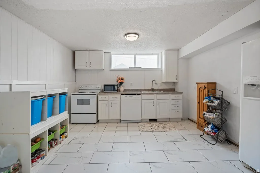 Kitchen featuring white appliances, a textured ceiling, white cabinetry, and light marble finish floors