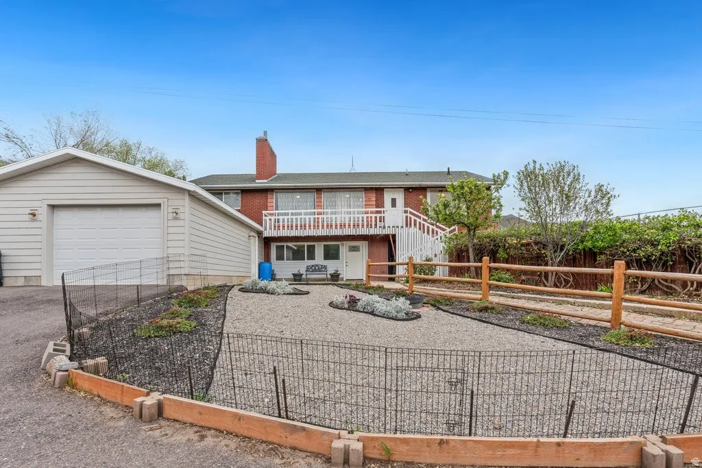 View of front of house featuring a garden, driveway, a chimney, brick siding, and a balcony