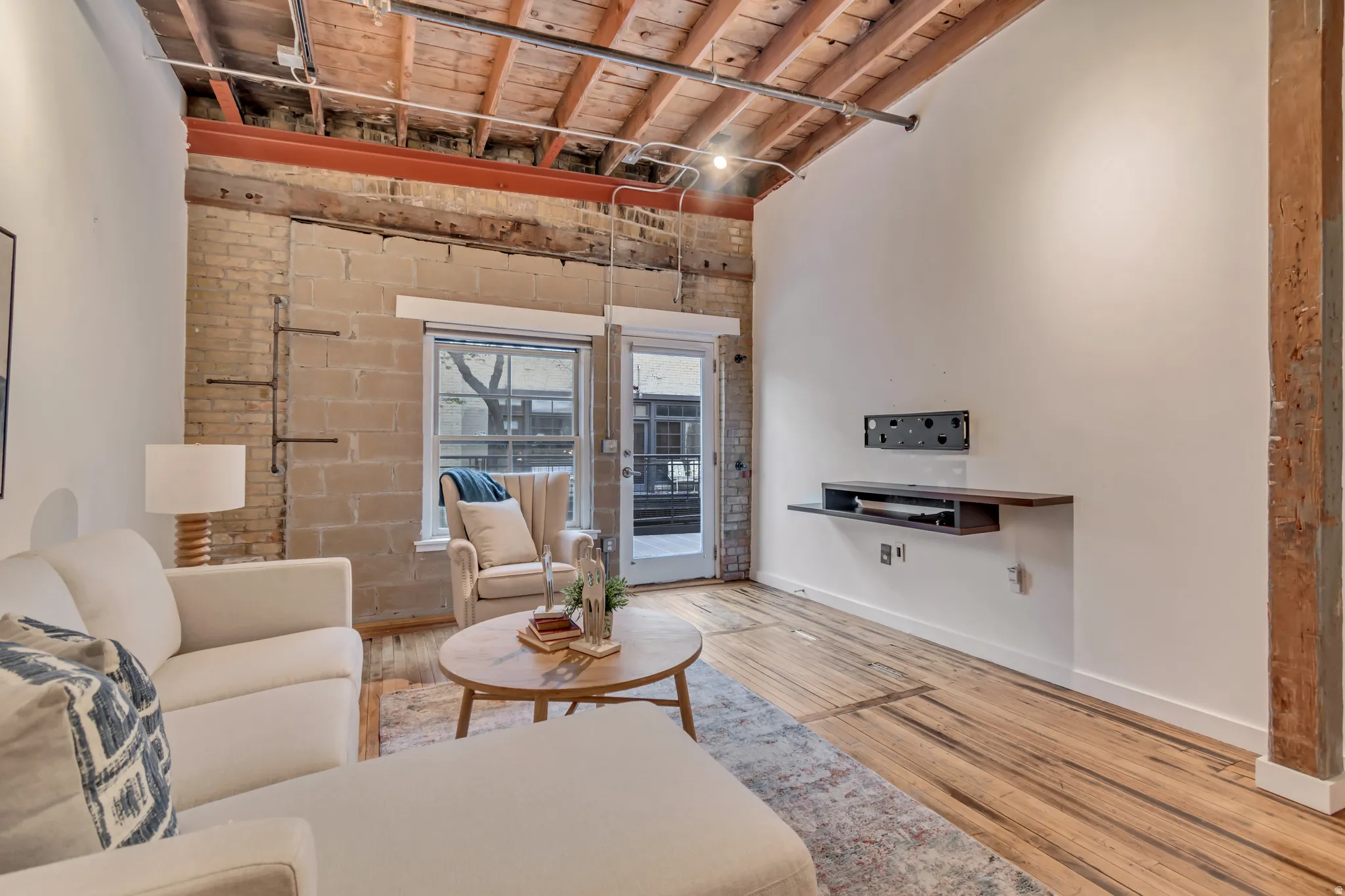 Living room featuring brick wall, light wood-type flooring, and a wooden ceiling with exposed beams