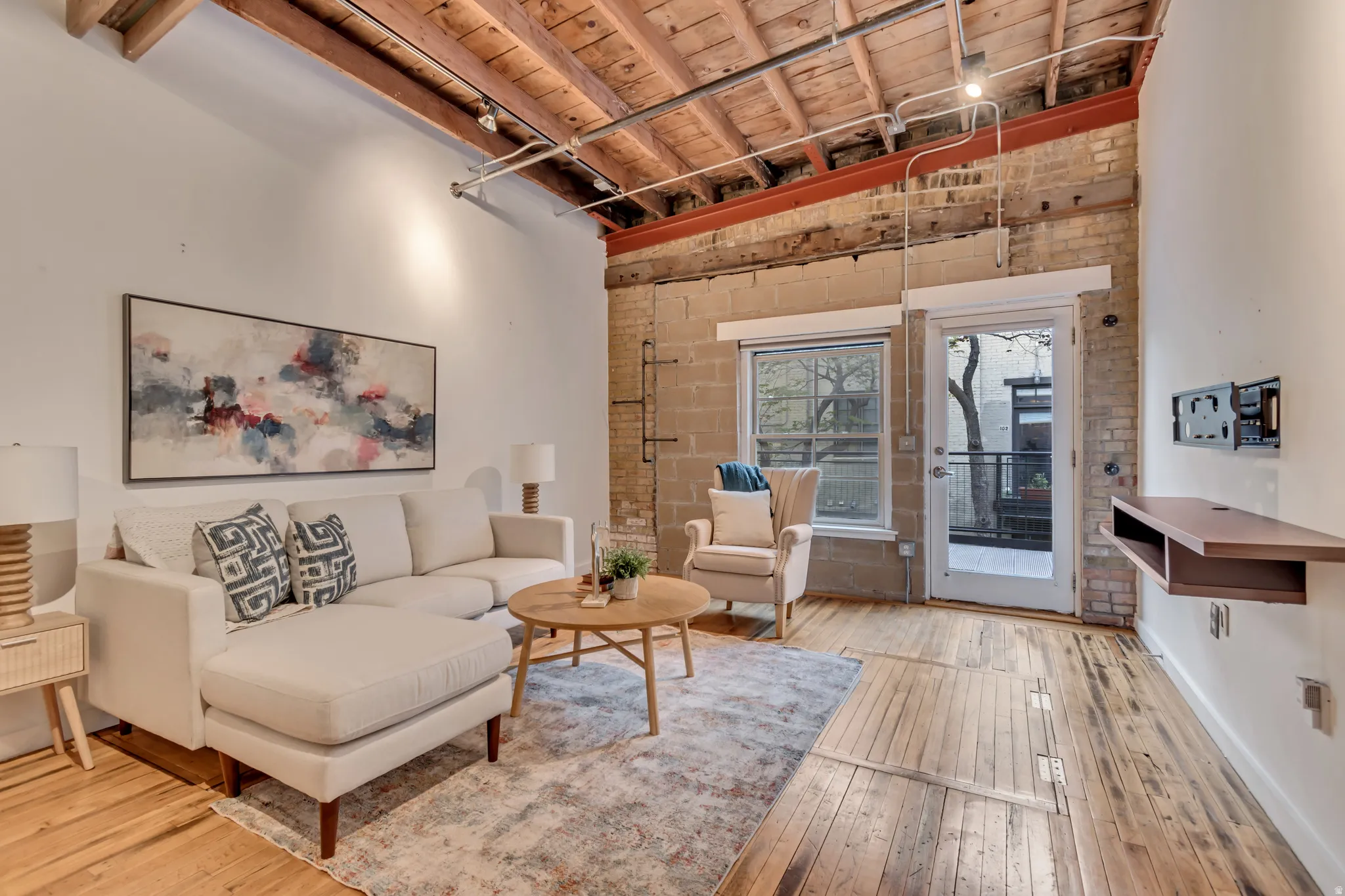 Living area with a high wooden beamed ceiling, light wood-style floors, brick wall, and rail lighting