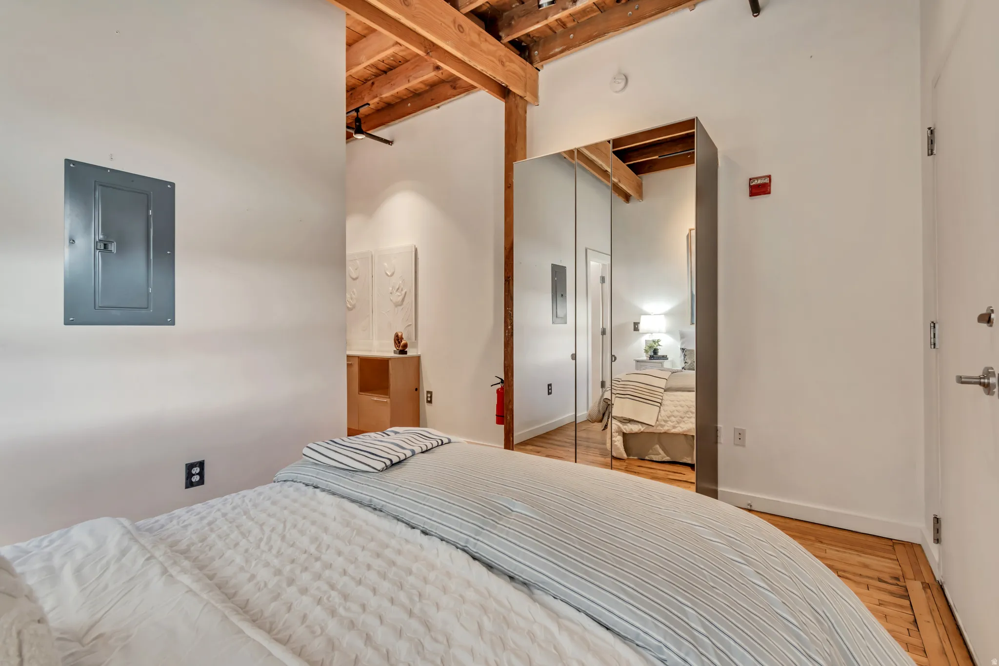 Bedroom with electric panel, light wood-style flooring, a wooden ceiling with exposed beams, and connected bathroom