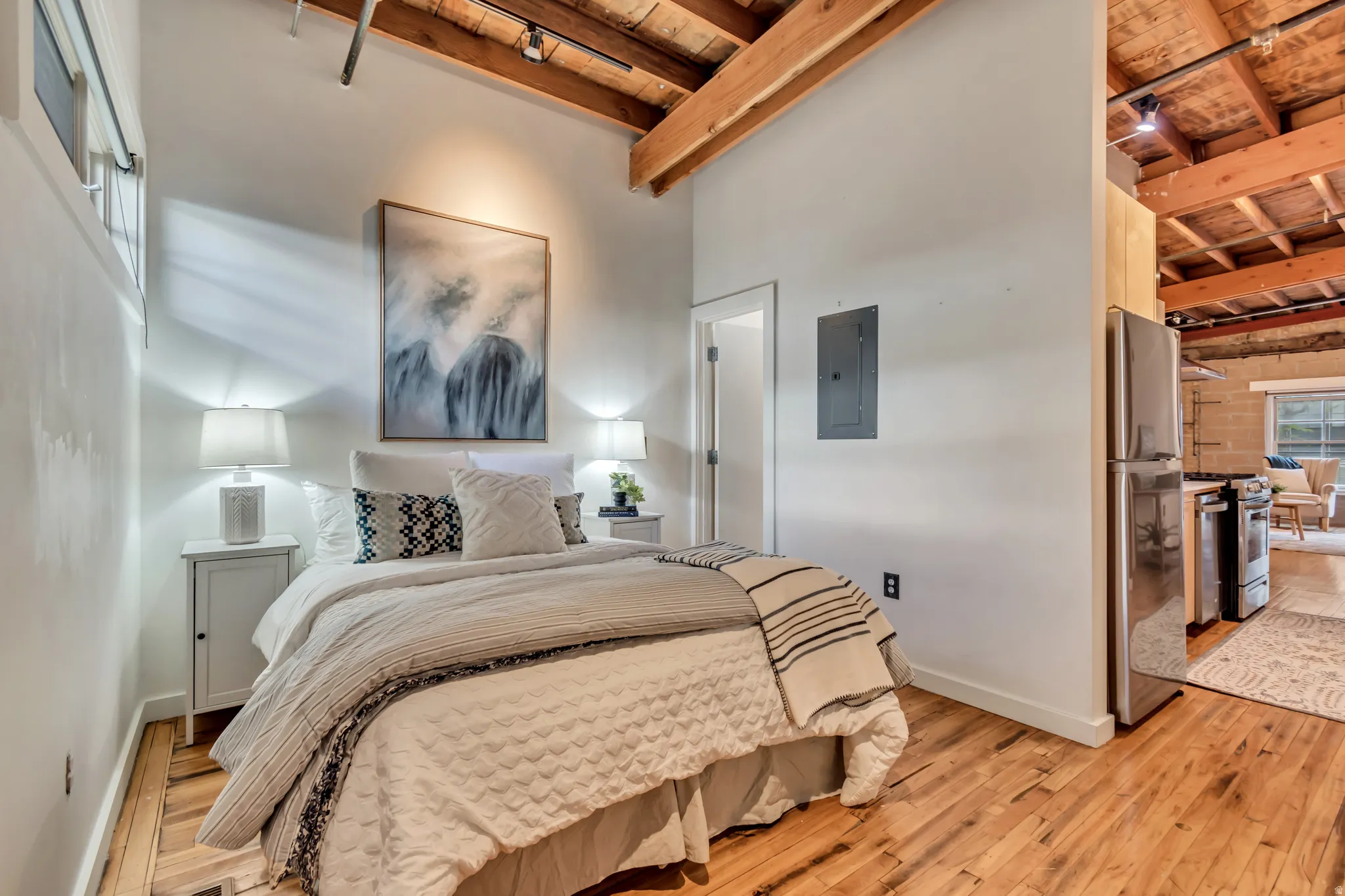 Bedroom featuring a high wood beamed ceiling, light wood-type flooring, freestanding refrigerator, electric panel, and track lighting