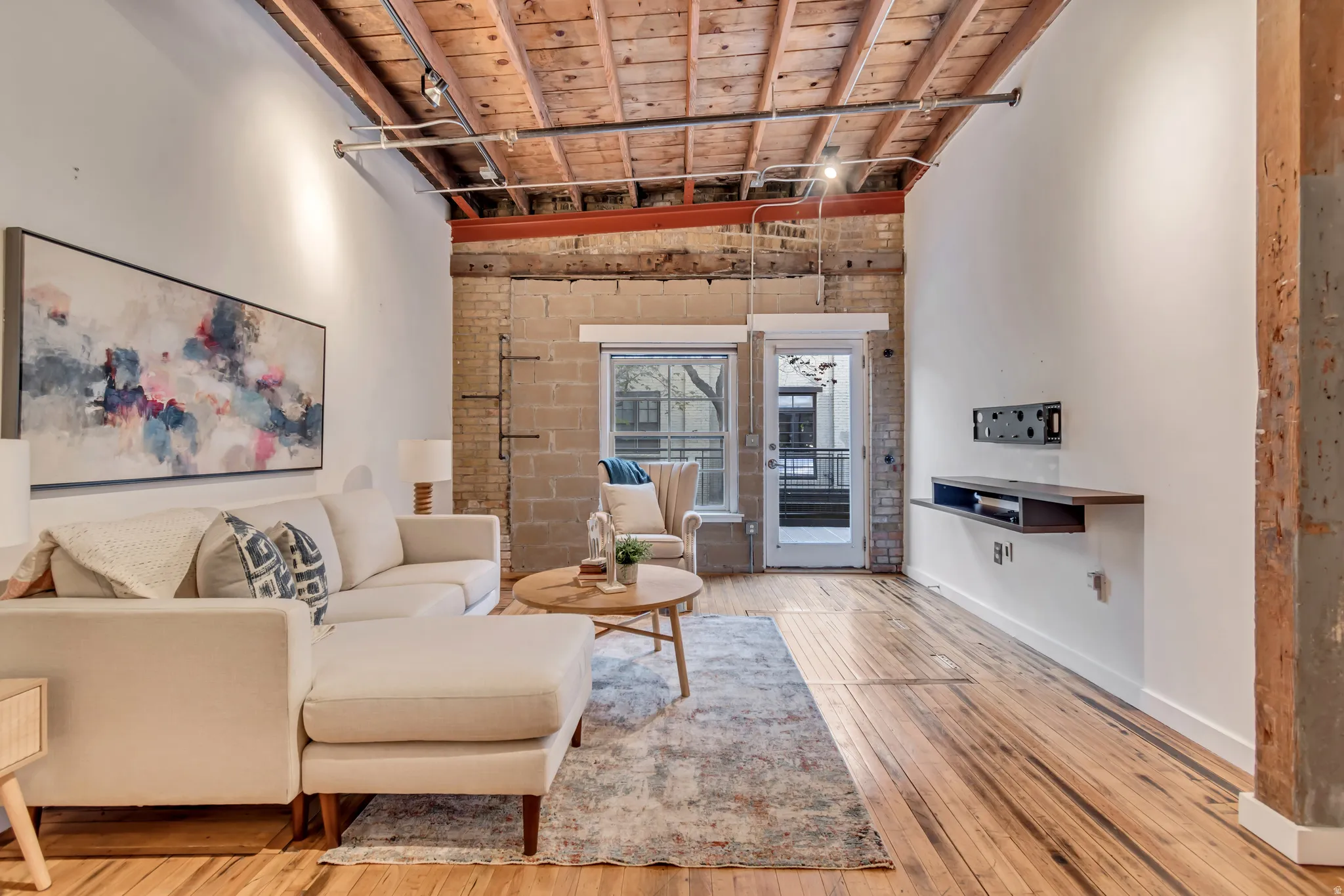 Living room featuring brick wall, light wood finished floors, a high wooden ceiling, and rail lighting