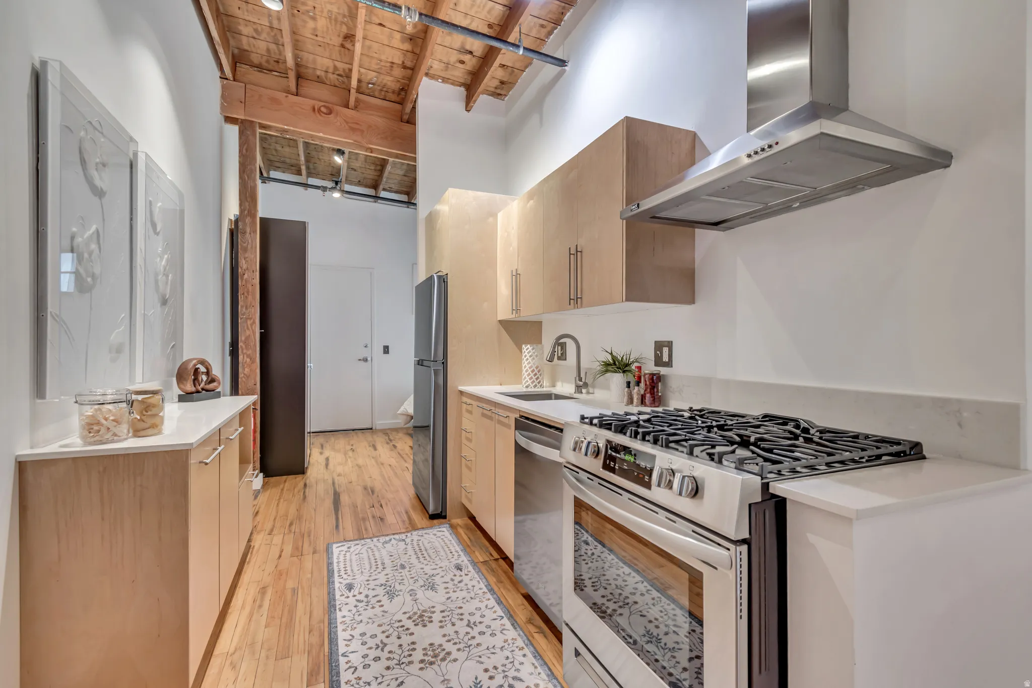 Kitchen featuring stainless steel appliances, a high wooden beamed ceiling, modern cabinets, and light wood finished floors