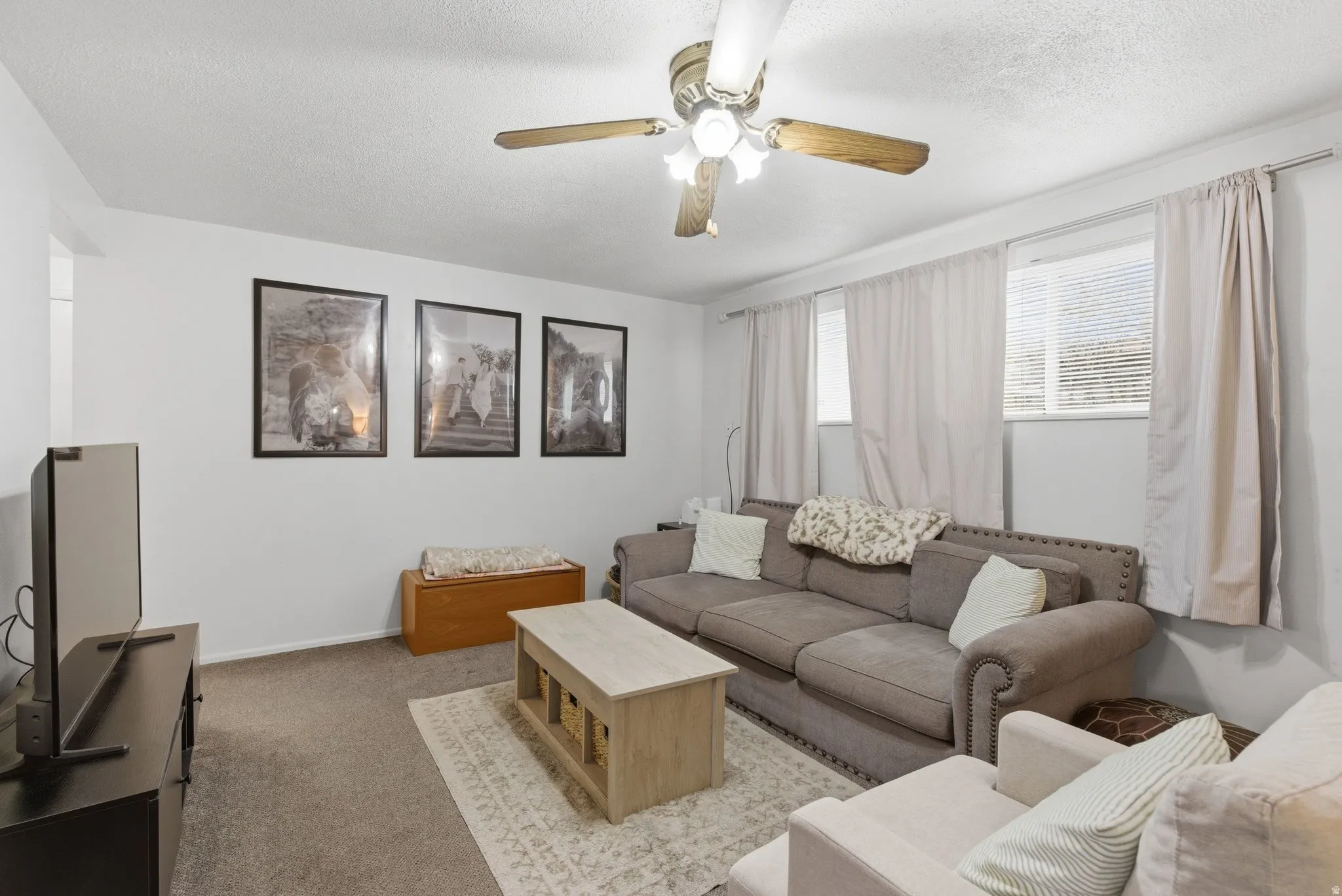 Carpeted living room featuring ceiling fan and a textured ceiling