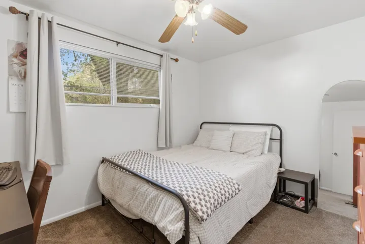 Bedroom with dark colored carpet, a ceiling fan, and arched walkways