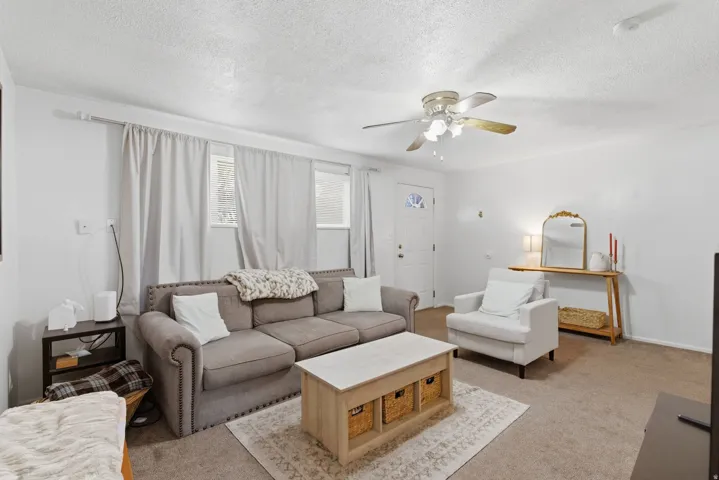Living area with carpet flooring, ceiling fan, and a textured ceiling