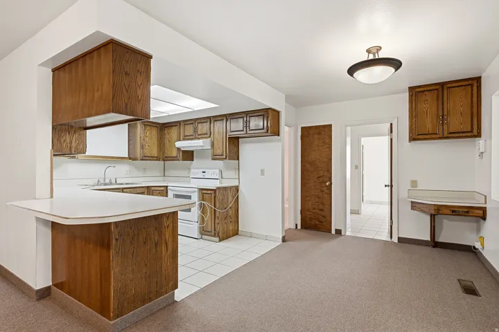 Kitchen with wood finish cabinets, light carpet, a peninsula, light countertops, and light tile patterned floors