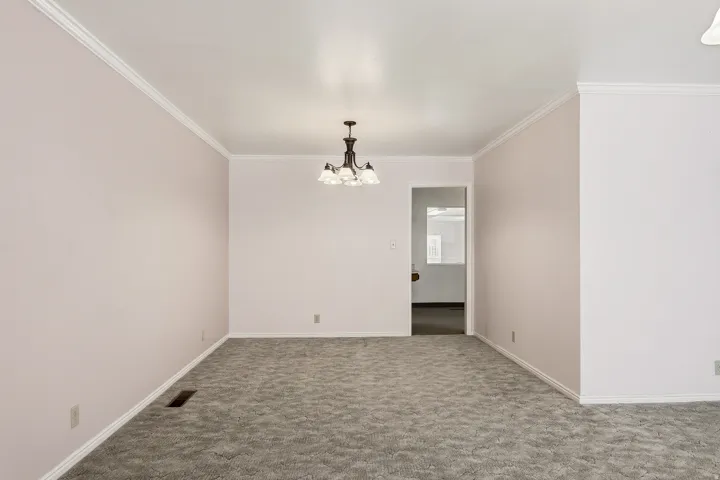 Carpeted spare room featuring ornamental molding and suspended lighting