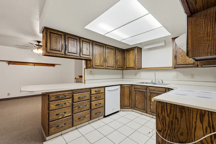 Kitchen with light countertops, white appliances, a peninsula, a ceiling fan, and light carpet