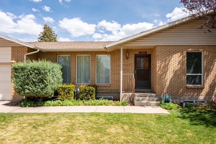 Doorway to property featuring a yard, brick siding, and roof with shingles
