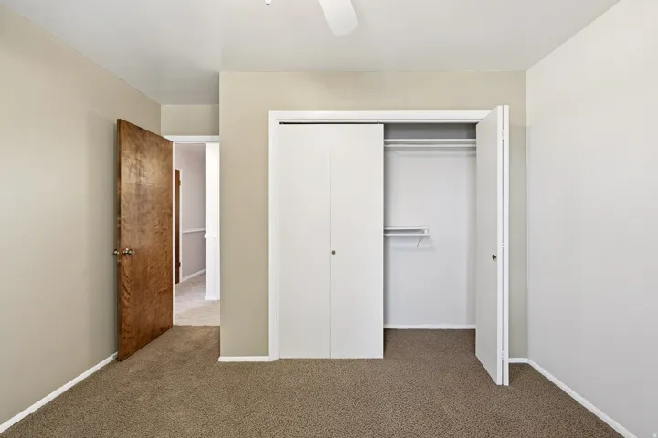 Unfurnished bedroom featuring dark carpet, a closet, and a ceiling fan