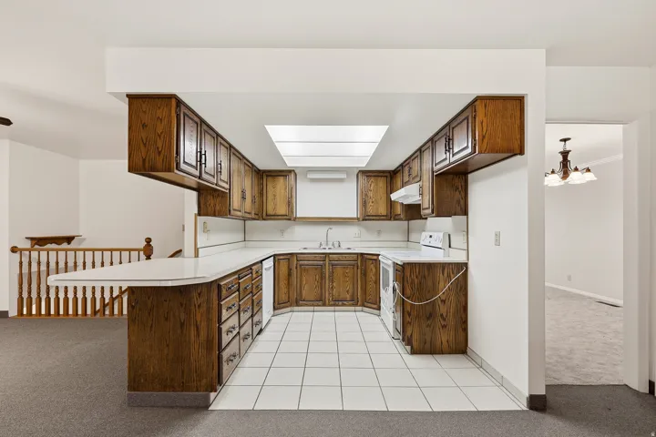 Kitchen with light colored carpet, light countertops, light tile patterned floors, white appliances, and a peninsula