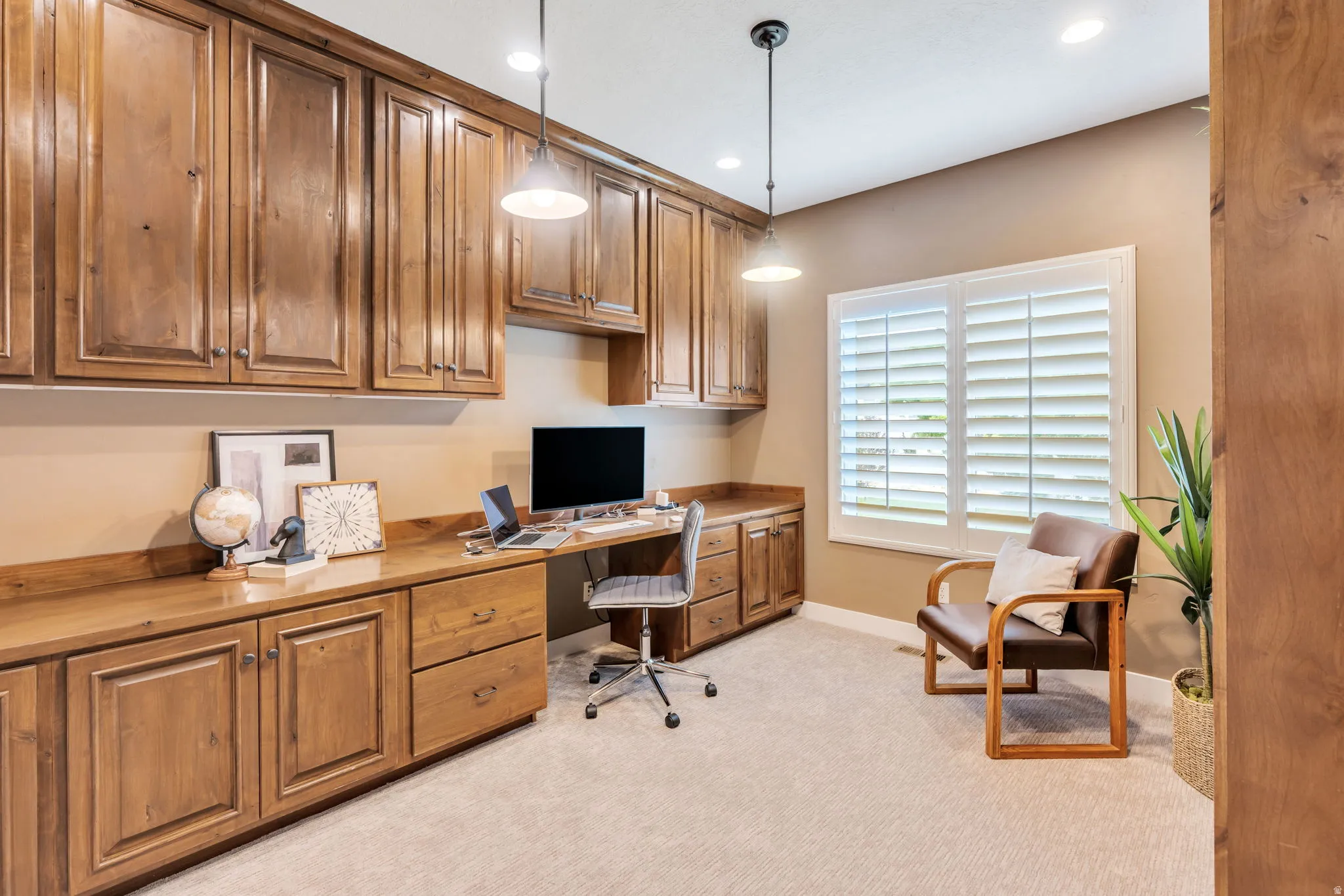 Dedicated office space featuring extensive wood cabinetry and integrated desk, pendant lighting, recessed ceiling lights, and window with plantation shutters