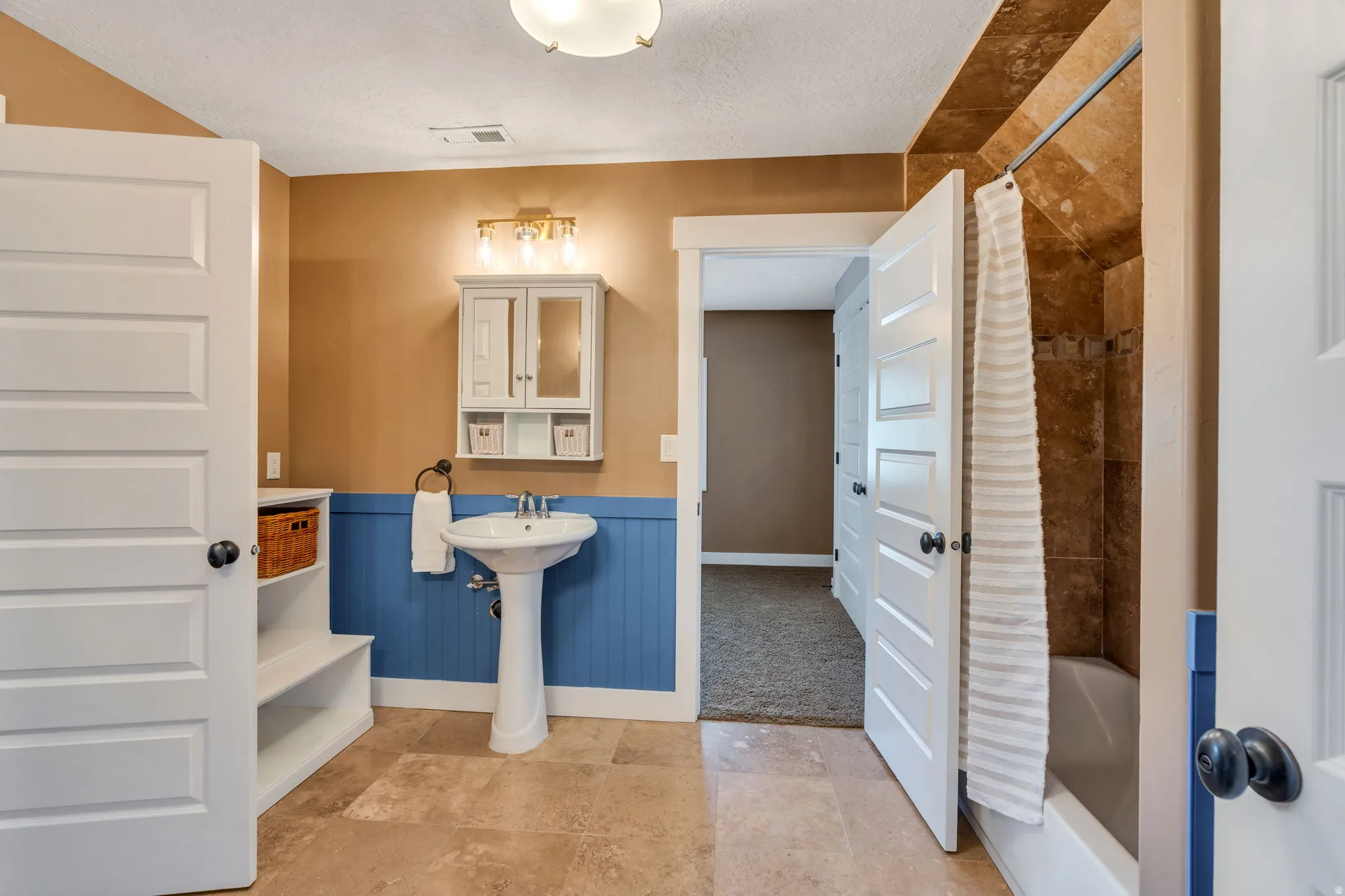 Bathroom with a wainscoted wall, a textured ceiling, and shower / bath combination with curtain
