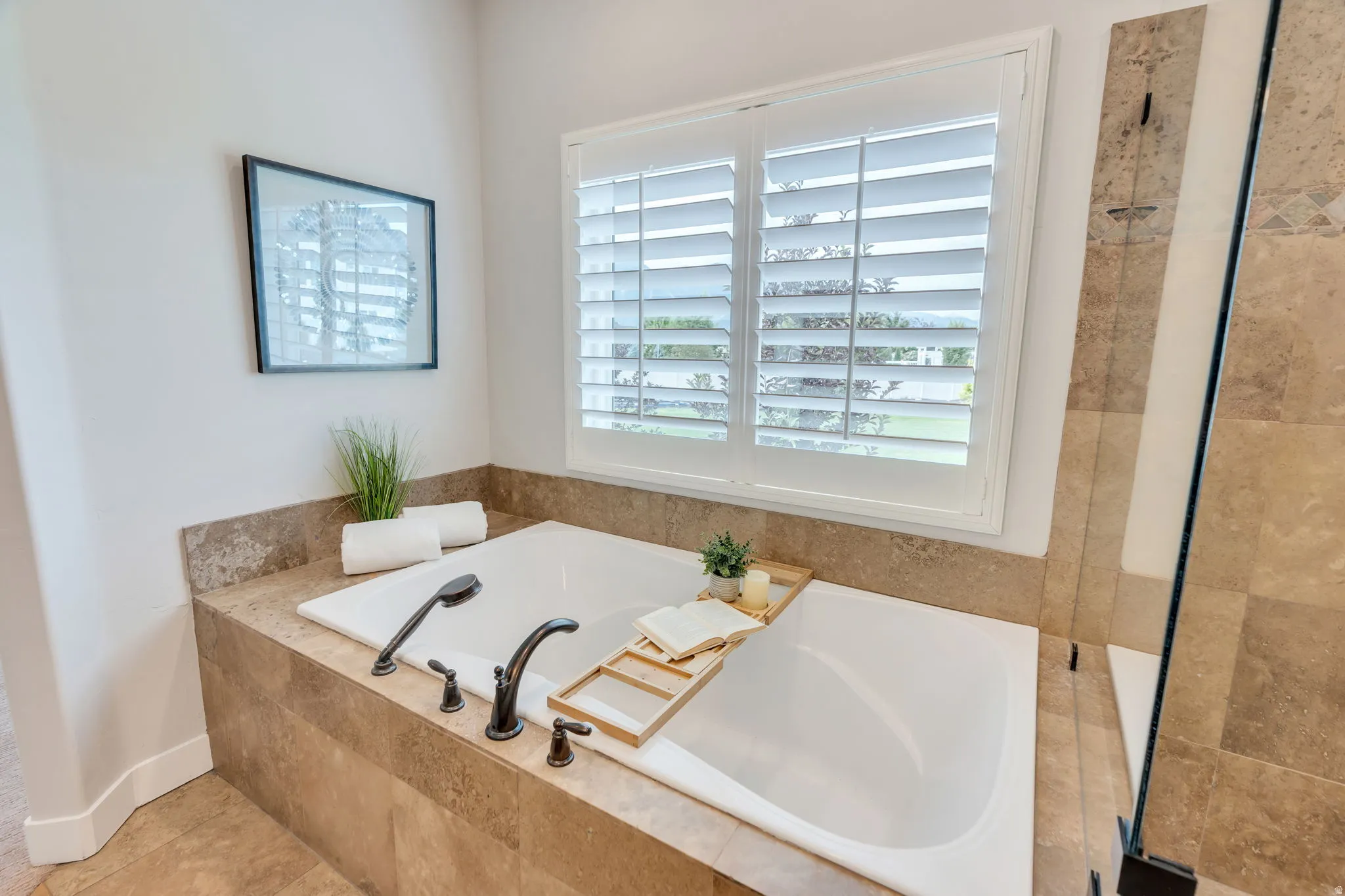 Built-in bathtub with dark bronze fixtures, surrounded by a stone-tiled enclosure and matching countertop