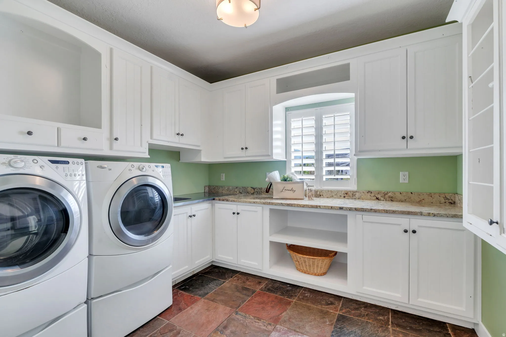 Dedicated laundry room featuring extensive white cabinetry, granite-style countertops, and multi-toned slate-look floor tiling