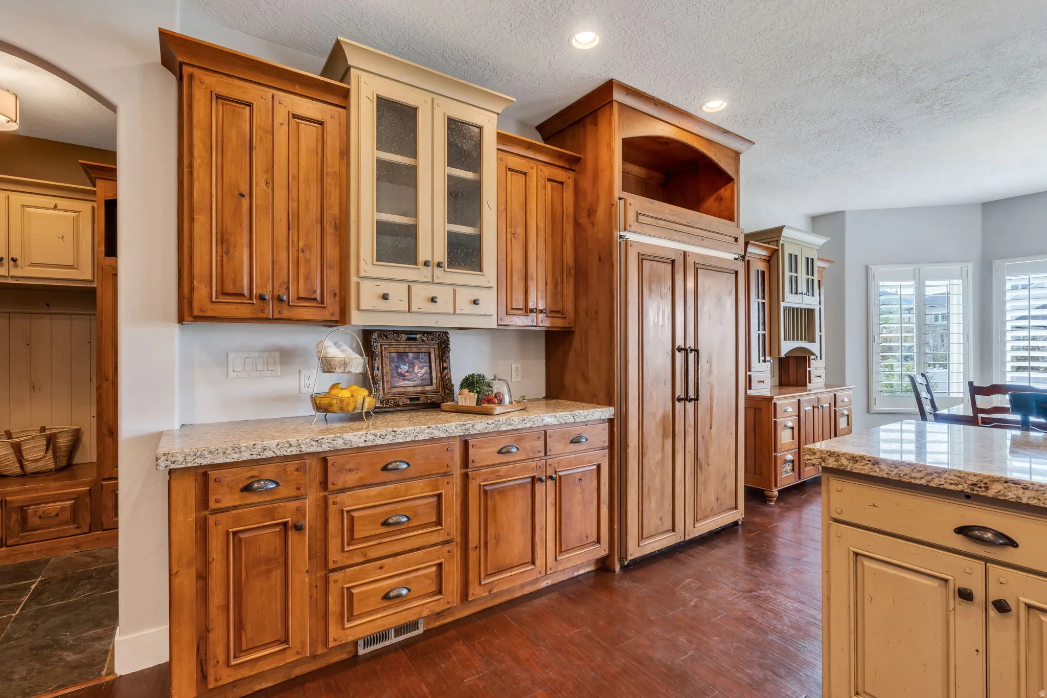 Kitchen featuring glass insert cabinets, paneled built in refrigerator, wood finish cabinets, light stone countertops, and a textured ceiling