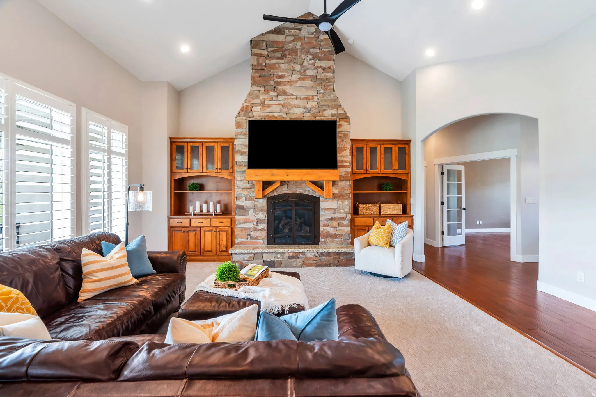 Carpeted living room with a ceiling fan, wood finished floors, a stone fireplace, and a high ceiling