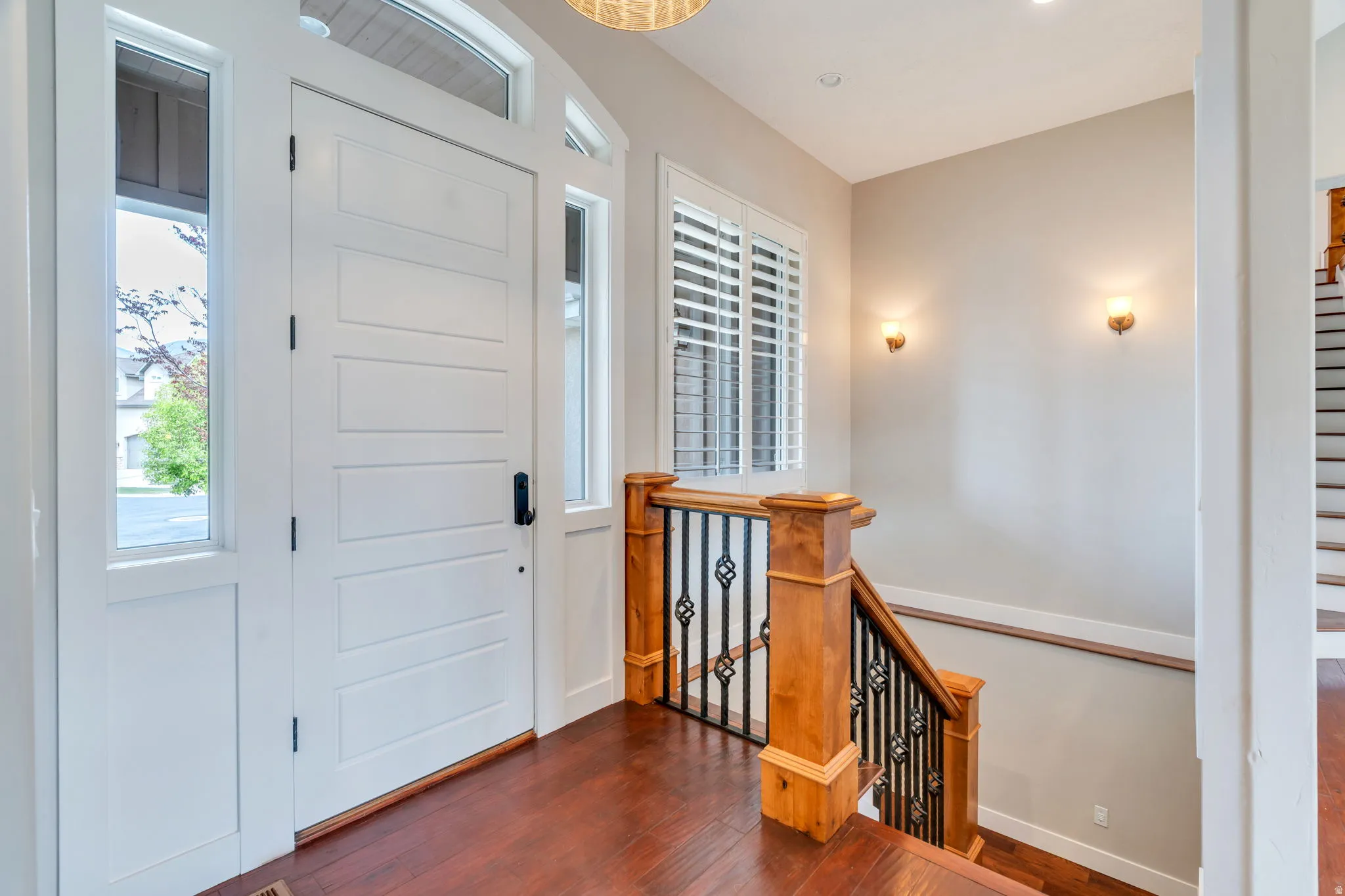 Entryway featuring a paneled white front door, sidelight windows, wood-finish flooring, and a staircase with an ornamental iron railing