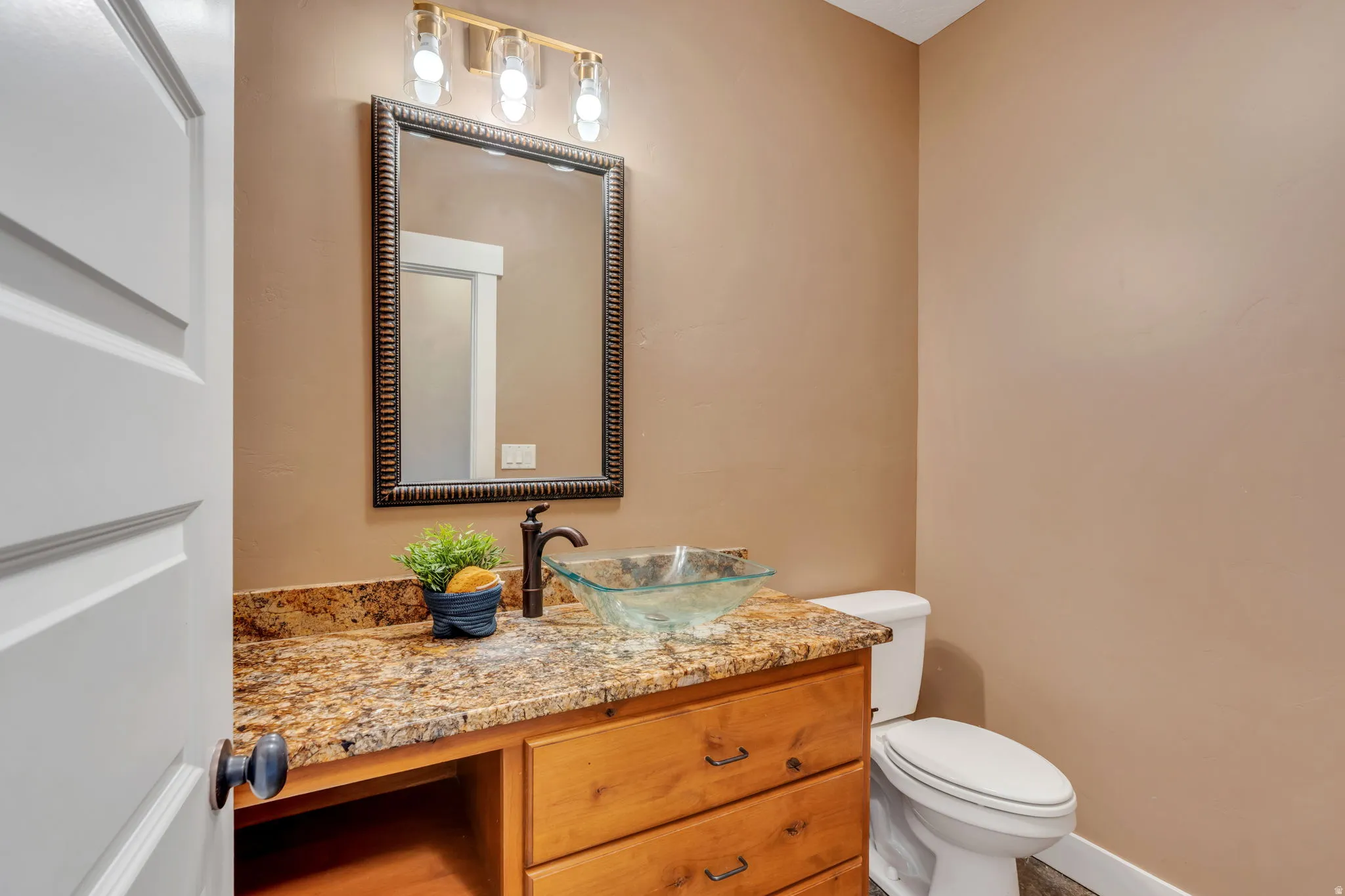 Bathroom featuring a wood vanity with integrated storage, a glass vessel sink, a dark bronze faucet, and a granite-style countertop