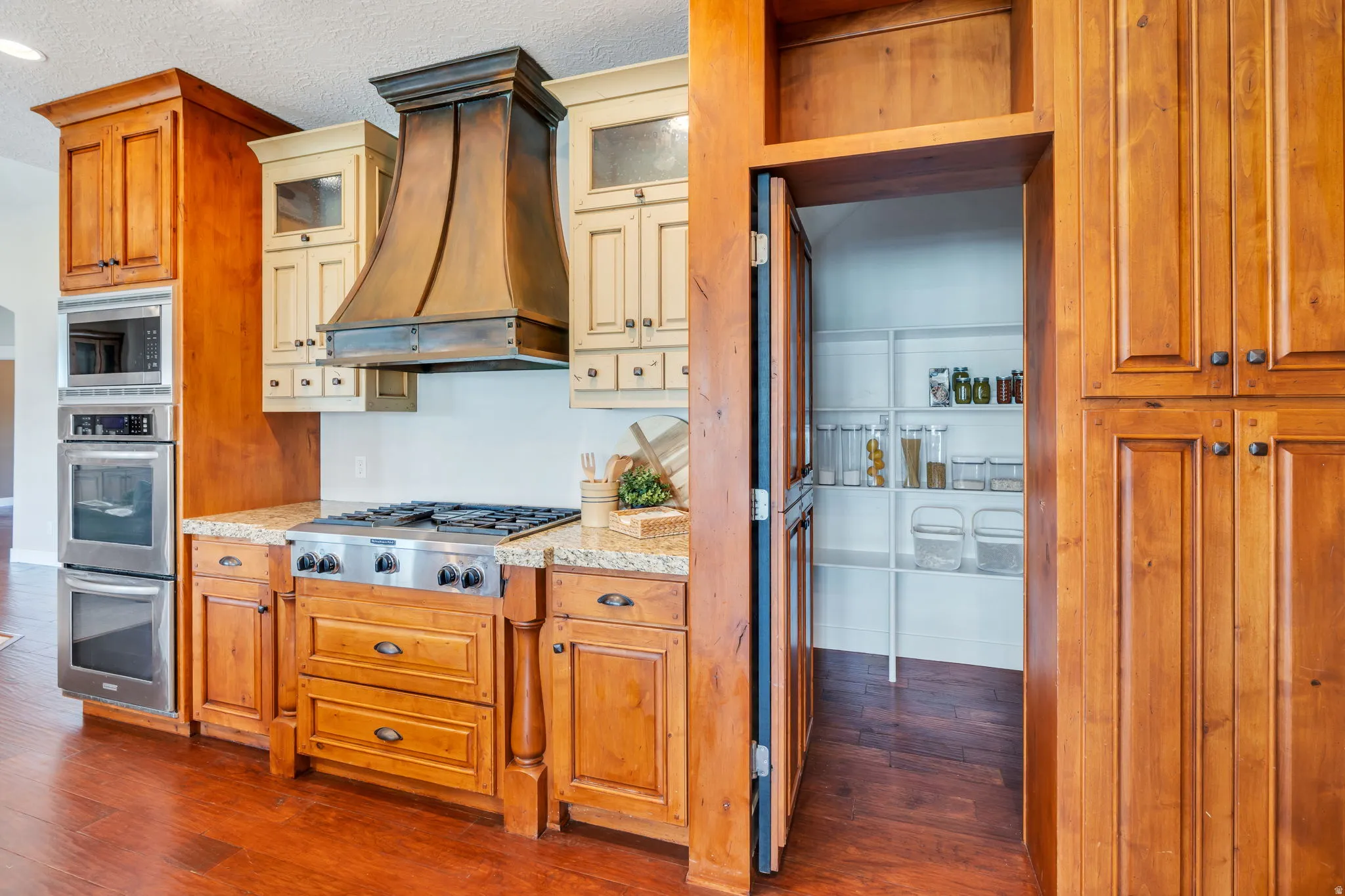 Gourmet kitchen featuring a built-in oven and microwave, a gas range with a custom range hood, wood cabinetry, granite countertops, and wood-finish flooring