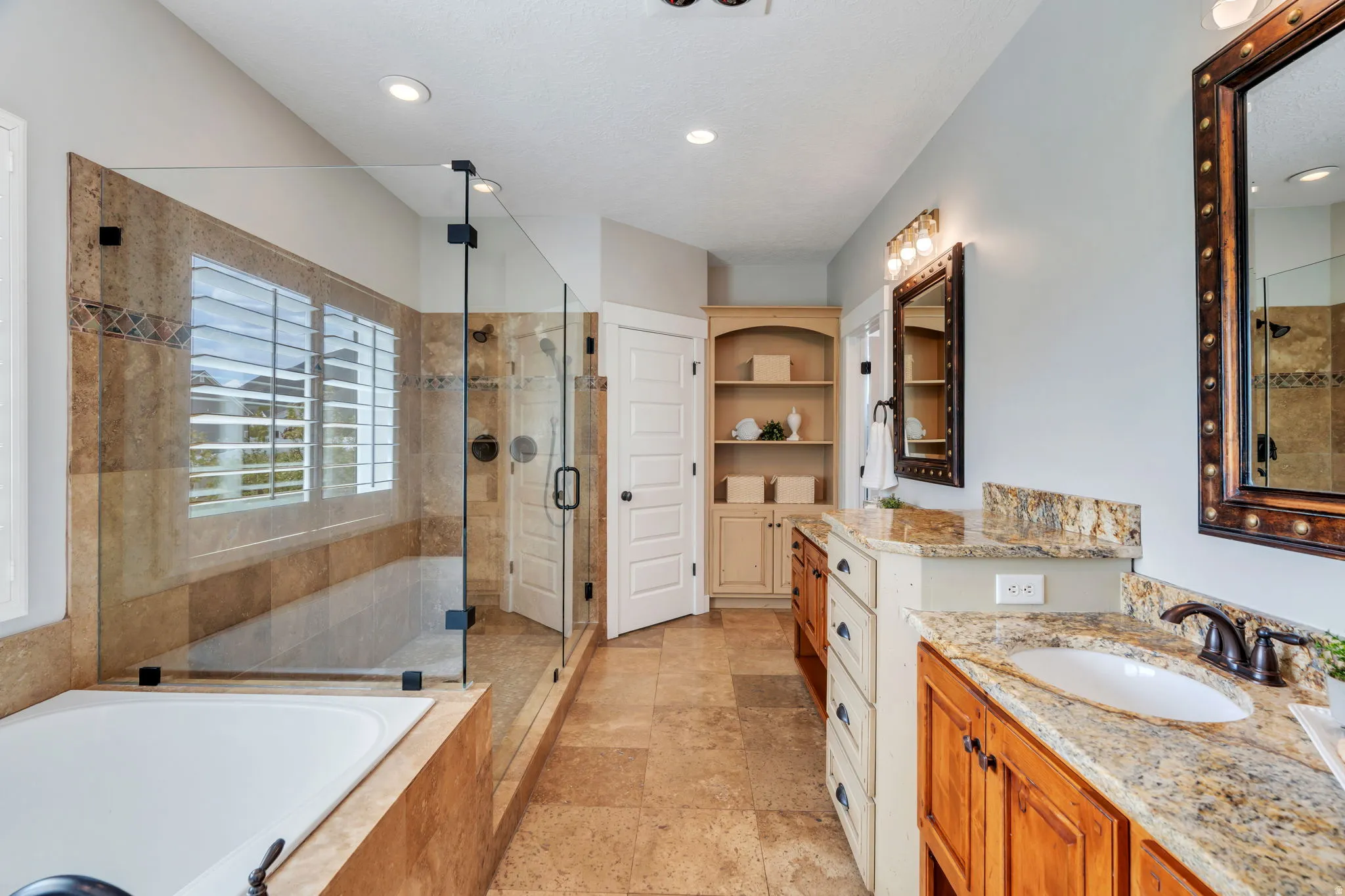 Full bath with two vanities, a stall shower, a garden tub, and light stone finish flooring