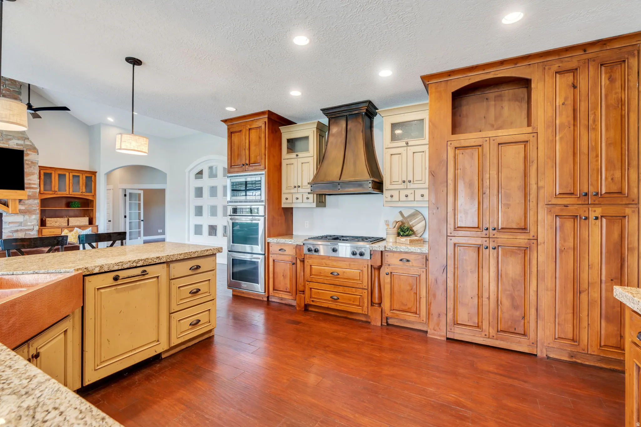 Two tone kitchen featuring arched walkways, hanging light fixtures, dark wood-style flooring, open floor plan, and light stone counters