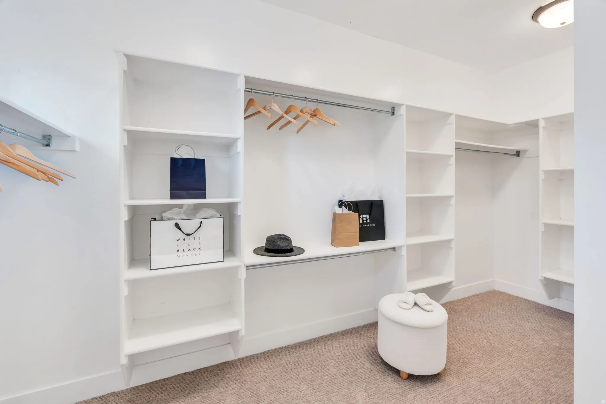 Built-in closet system featuring white shelving, multiple hanging rods, and light brown carpeting