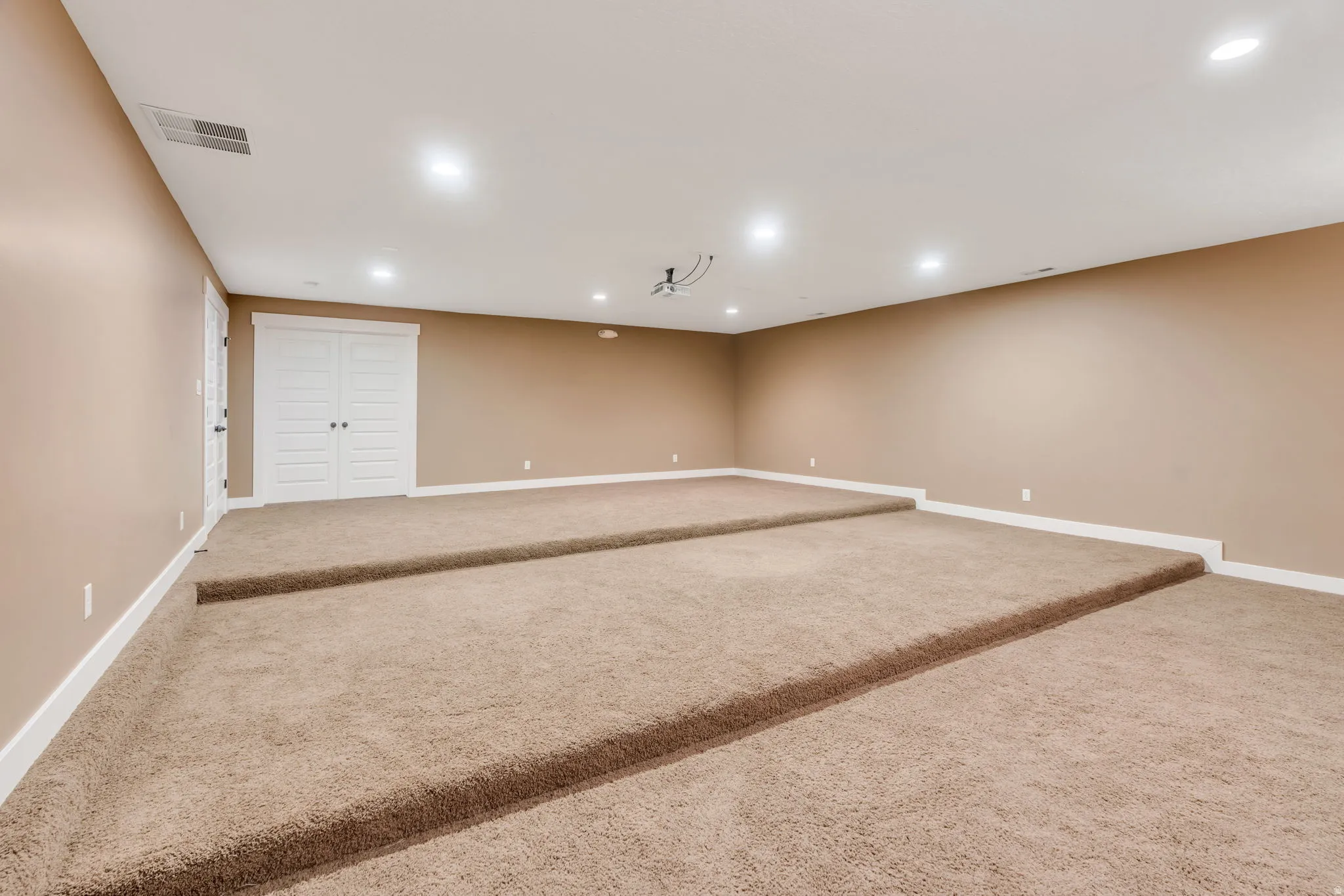 Spacious room with tiered, carpeted flooring, recessed lighting, and neutral wall tones