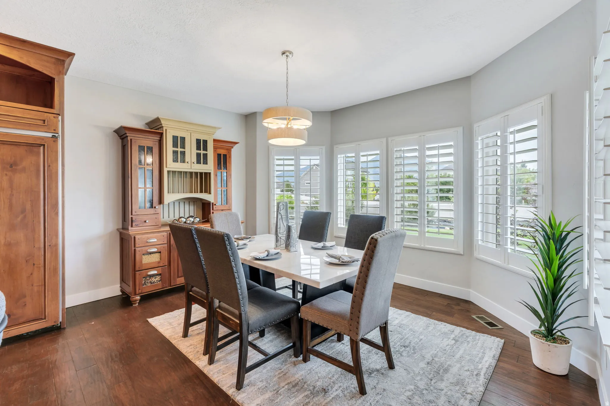 Dining area featuring wood-finish flooring, a contemporary chandelier, and a bay window with plantation shutters