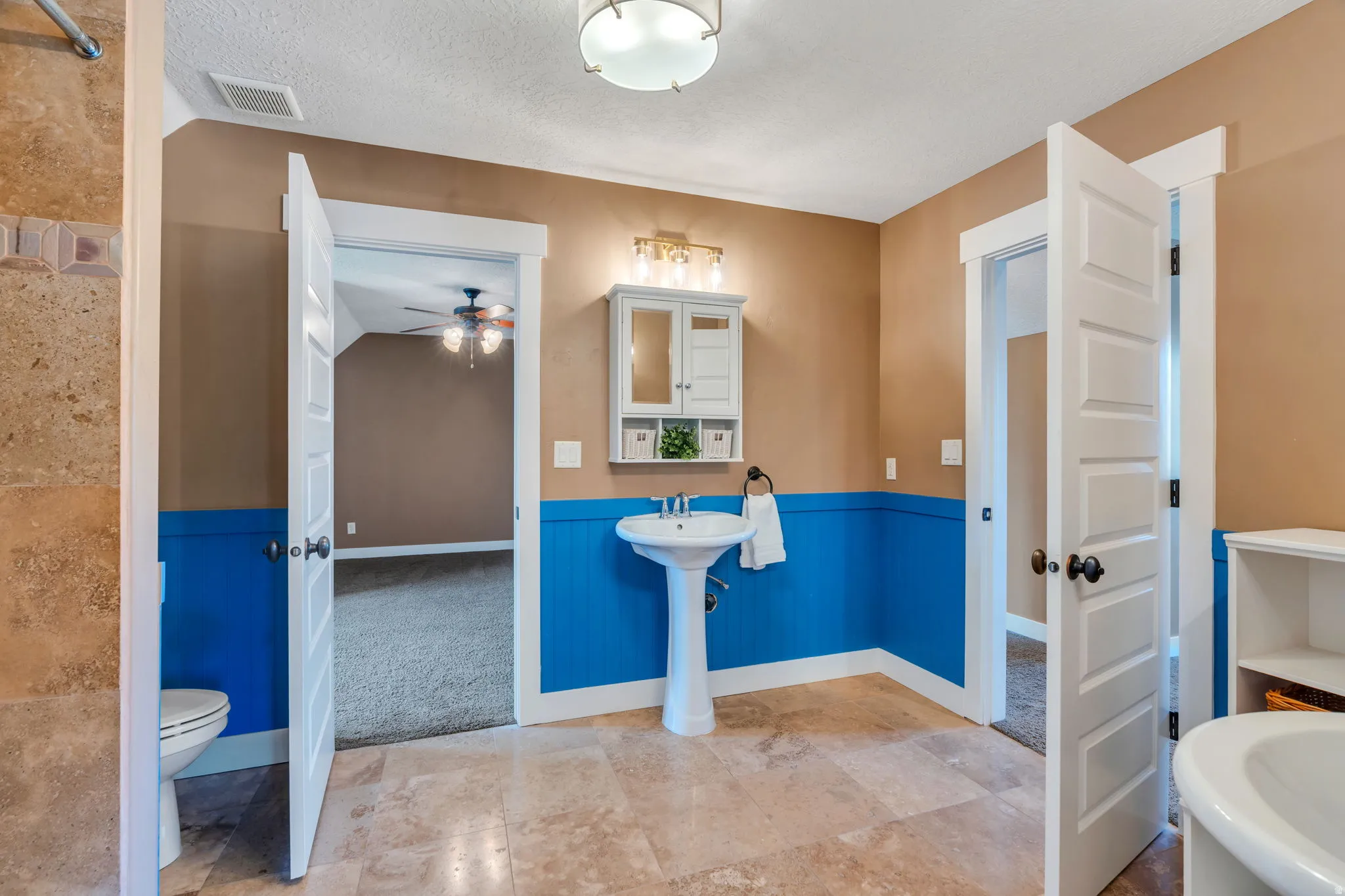 Full bathroom with a wainscoted wall, a textured ceiling, and ceiling fan