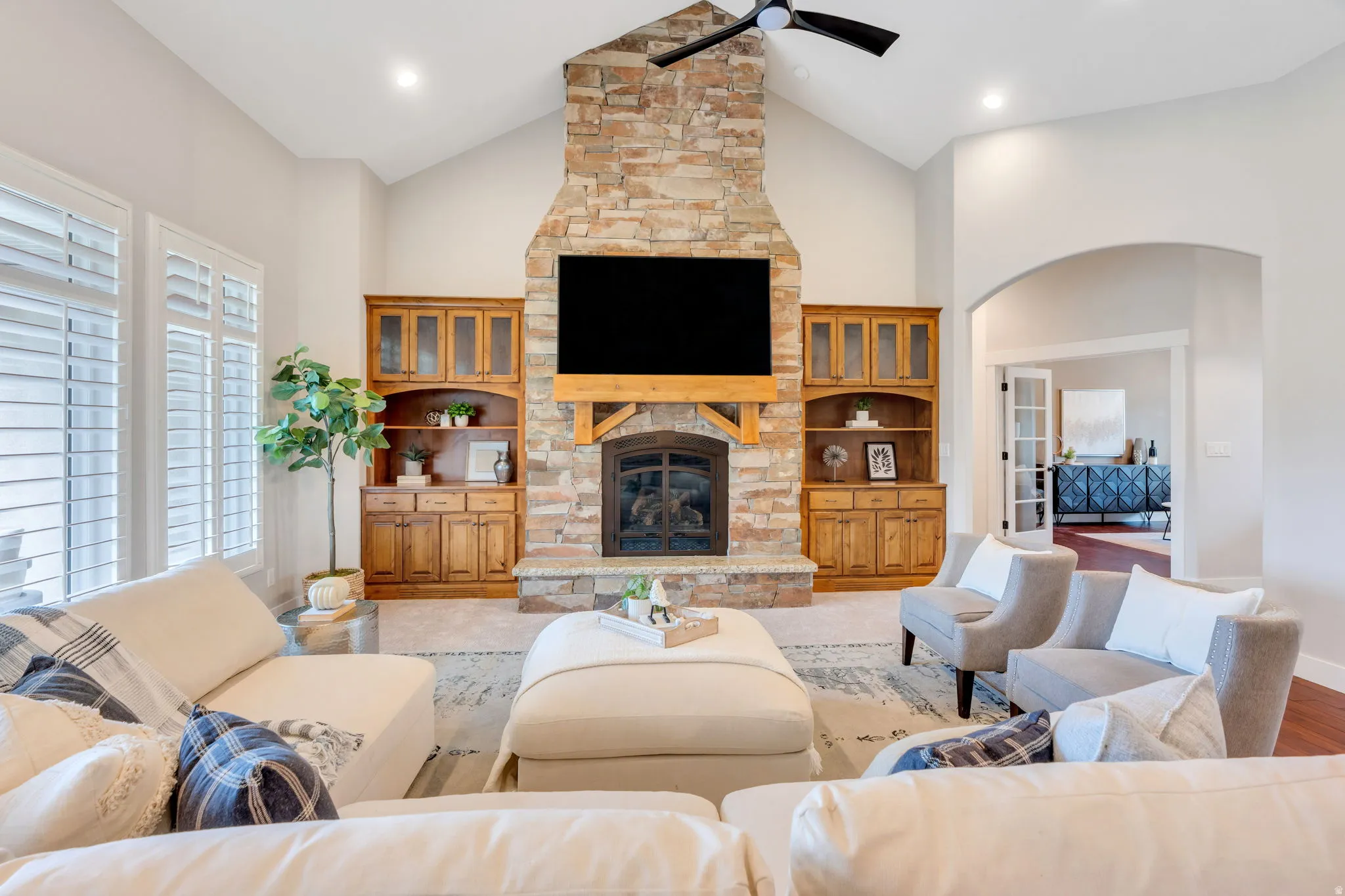 Vaulted ceiling living area featuring a stacked stone fireplace with wood mantel, built-in cabinetry, recessed lighting, and plantation shutters