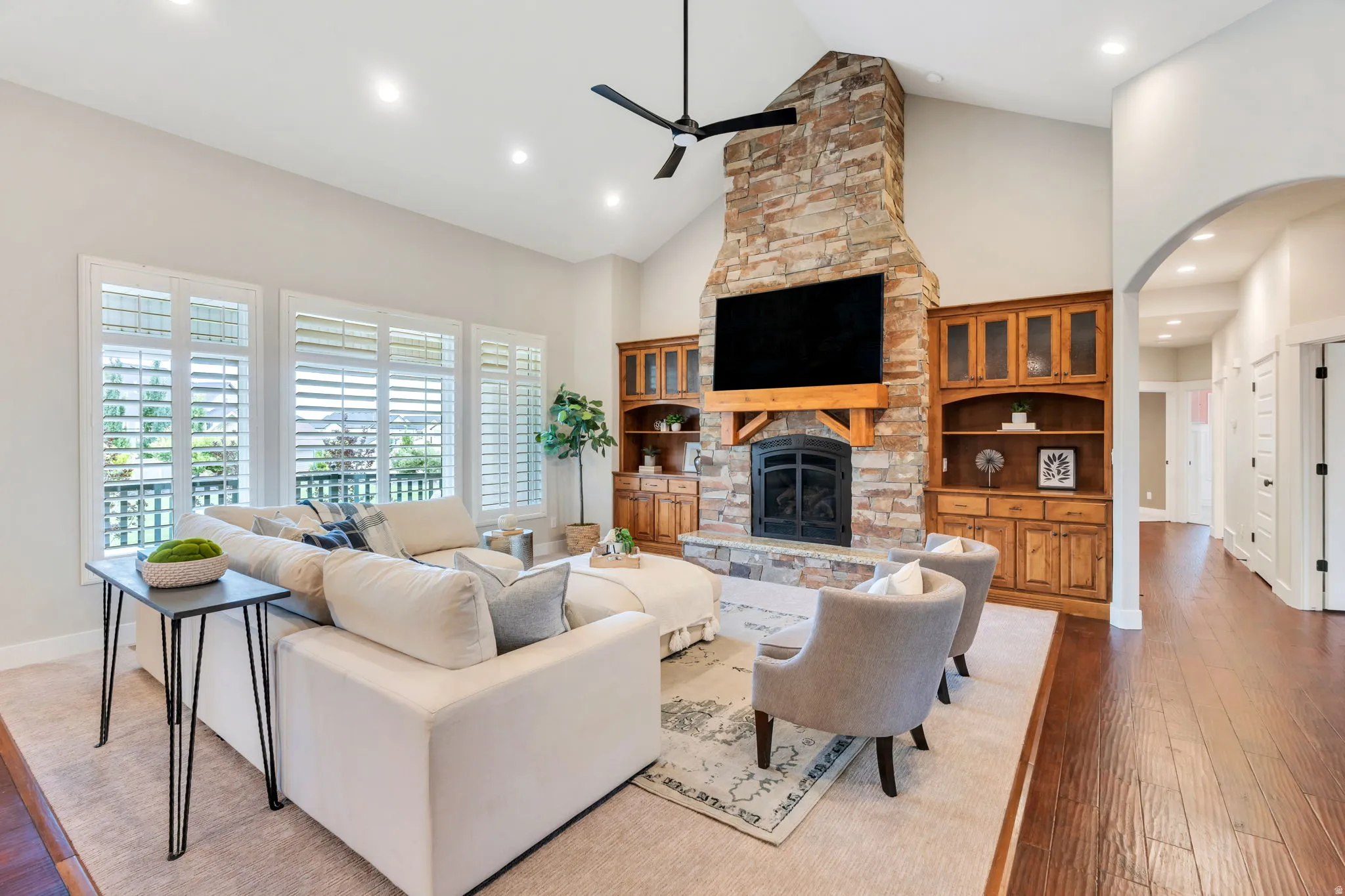 Spacious living area featuring a stone-clad fireplace with wood mantle, vaulted ceiling with recessed lighting, and built-in wood cabinetry