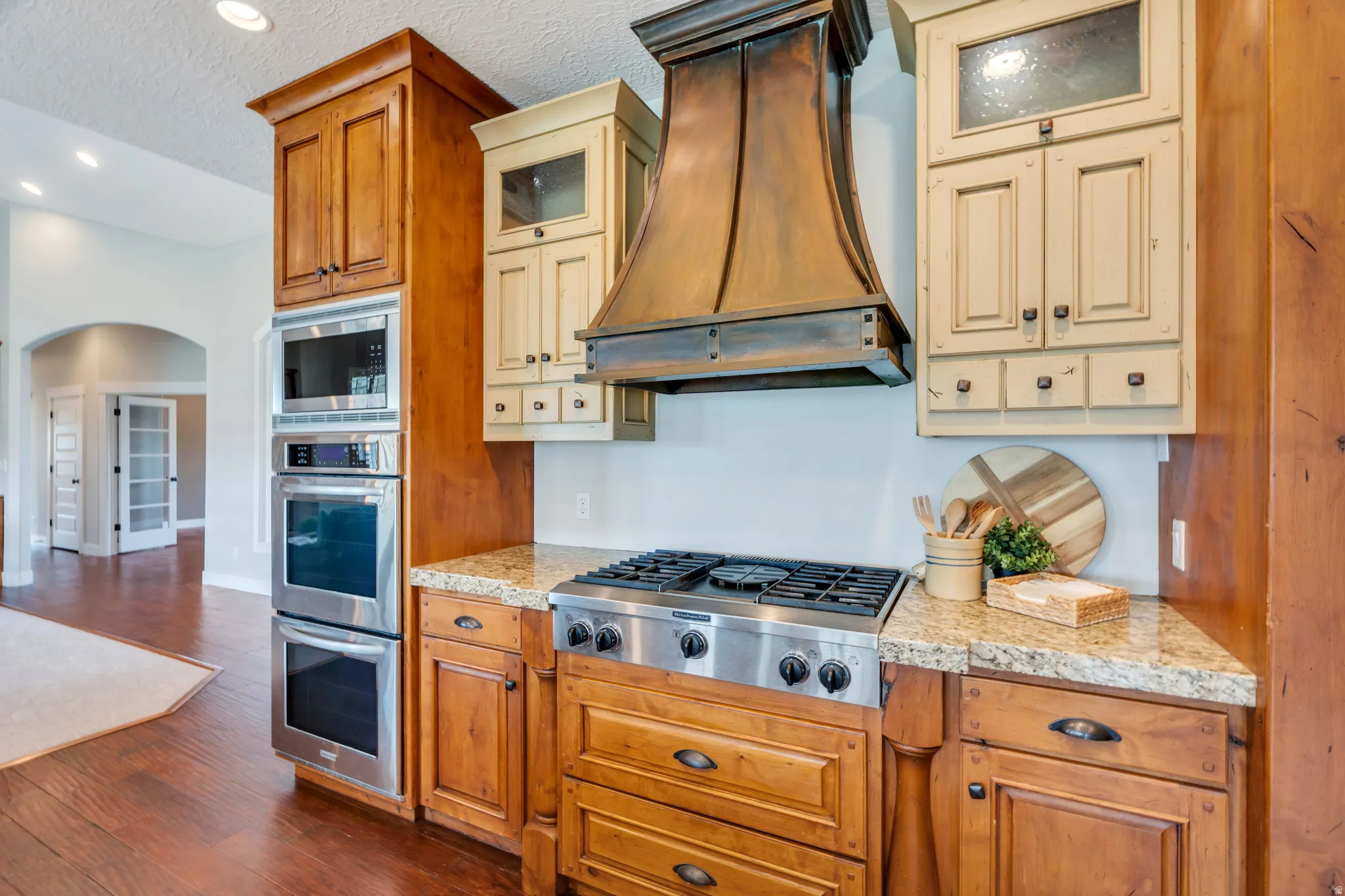 Kitchen with glass insert cabinets, stainless steel appliances, arched walkways, dark wood finished floors, and recessed lighting