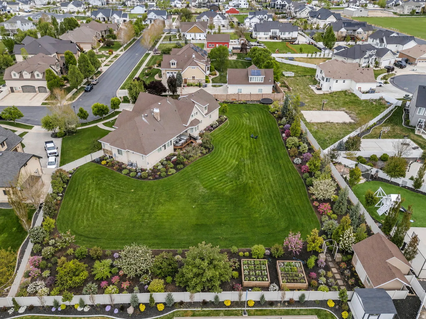 Expansive rear yard featuring a manicured lawn, lush landscaping, mature trees, and raised garden beds