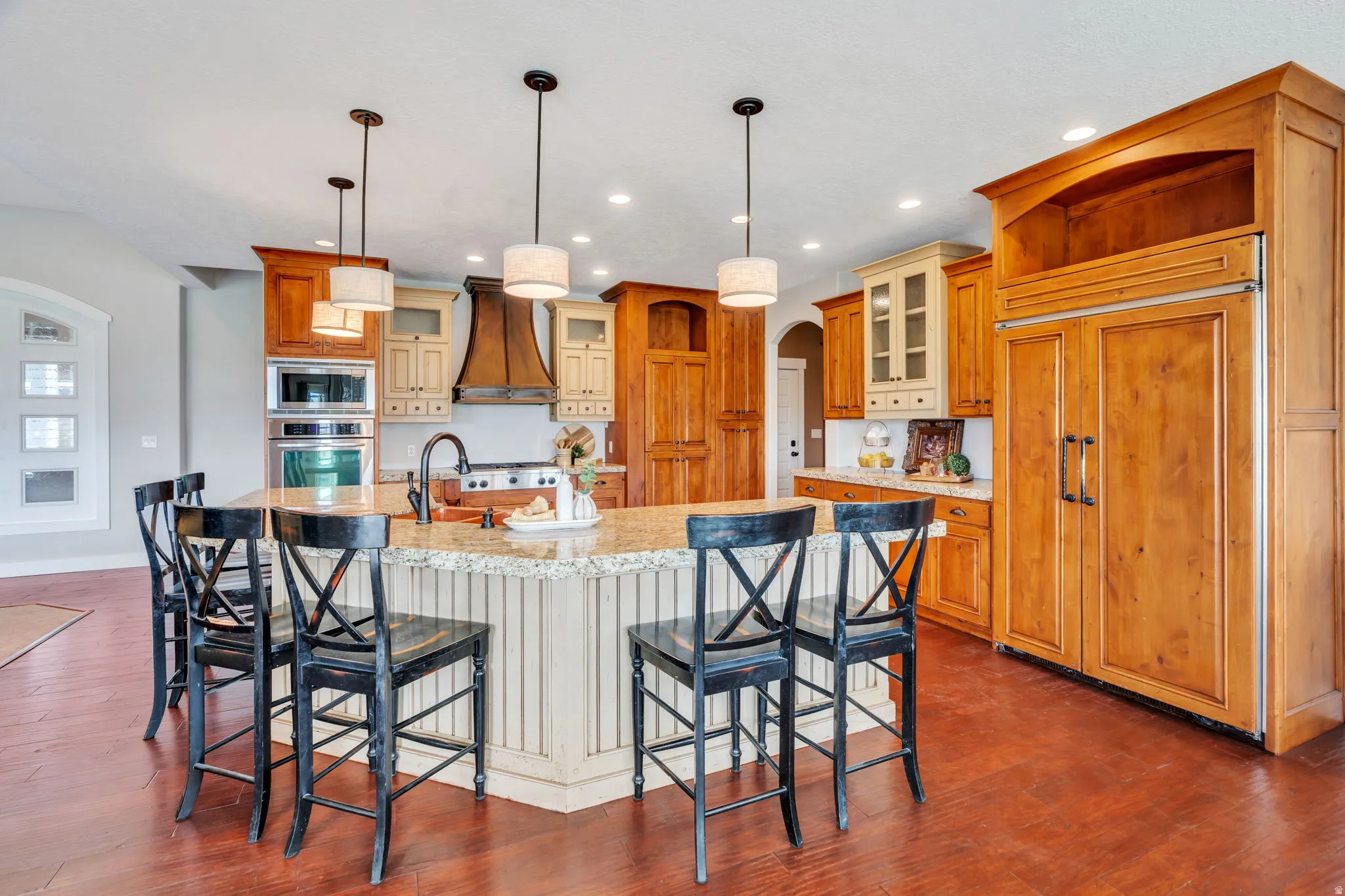 Kitchen featuring arched walkways, built in appliances, a kitchen bar, a spacious island, and dark wood-style floors