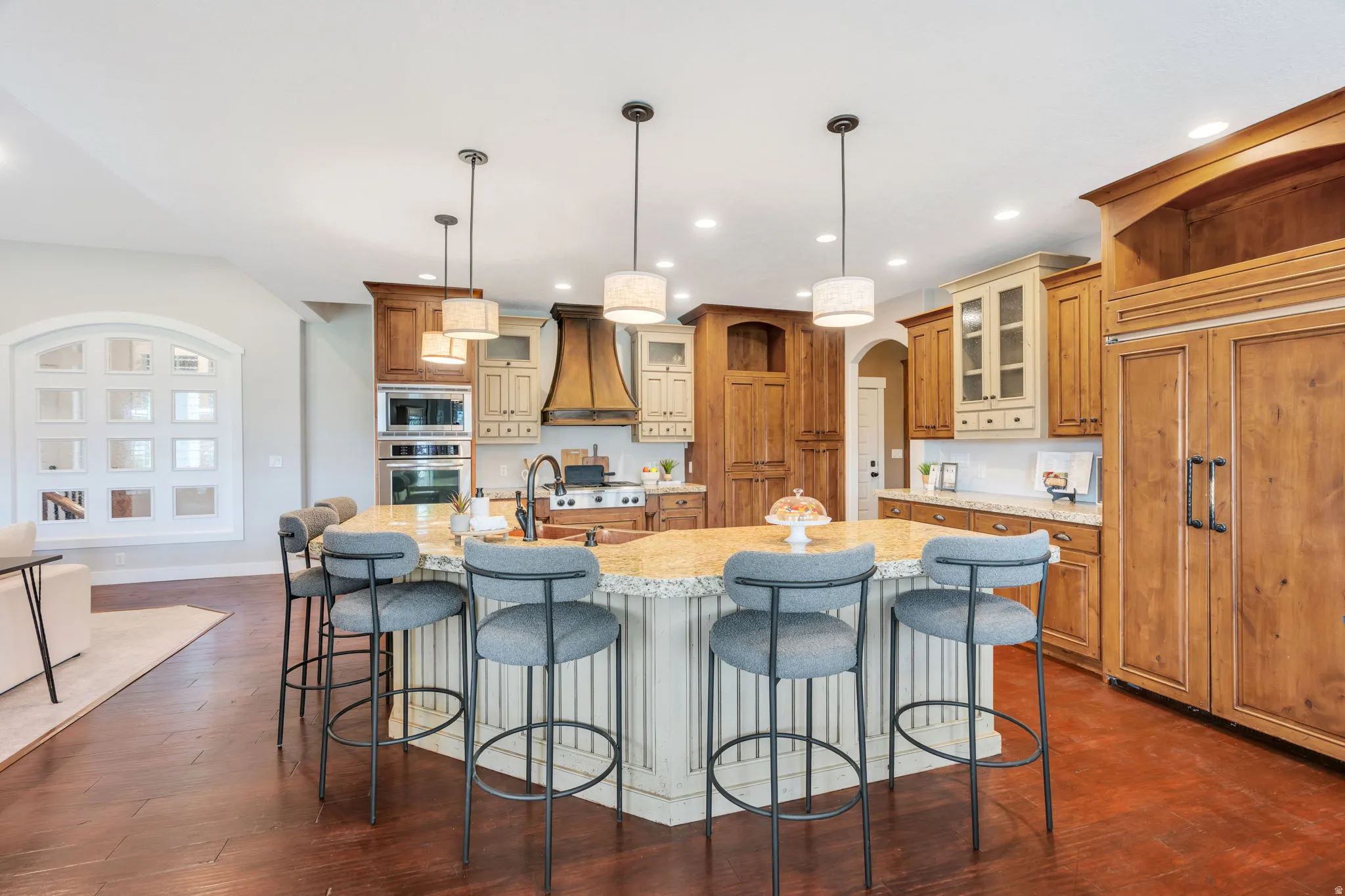 Spacious kitchen featuring a large central island with seating, a built-in double oven, paneled refrigeration, wood-finish cabinetry, and recessed lighting