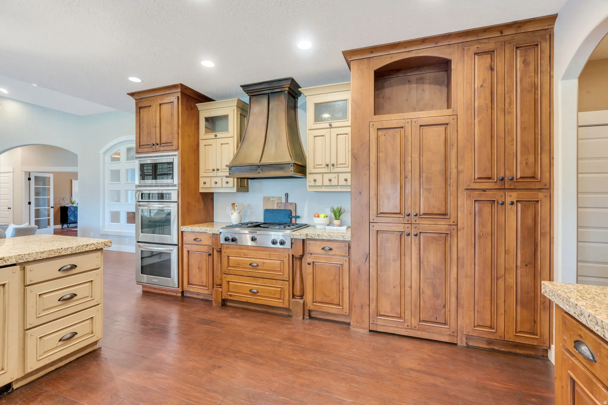 Gourmet kitchen featuring a professional-grade range, double wall ovens, a custom range hood, extensive wood cabinetry, and granite countertops