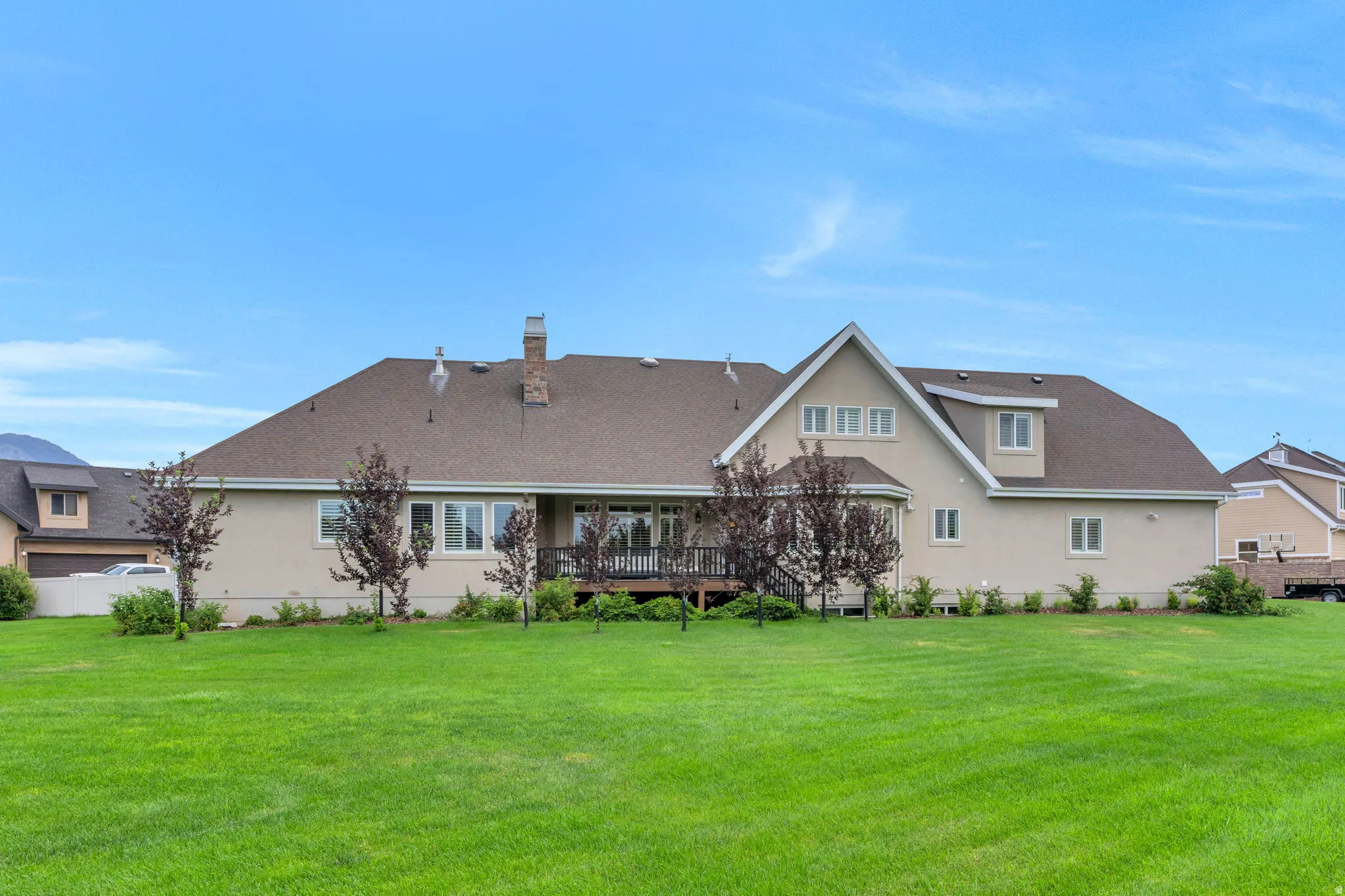 Expansive rear yard featuring a manicured lawn, mature trees, and a spacious deck