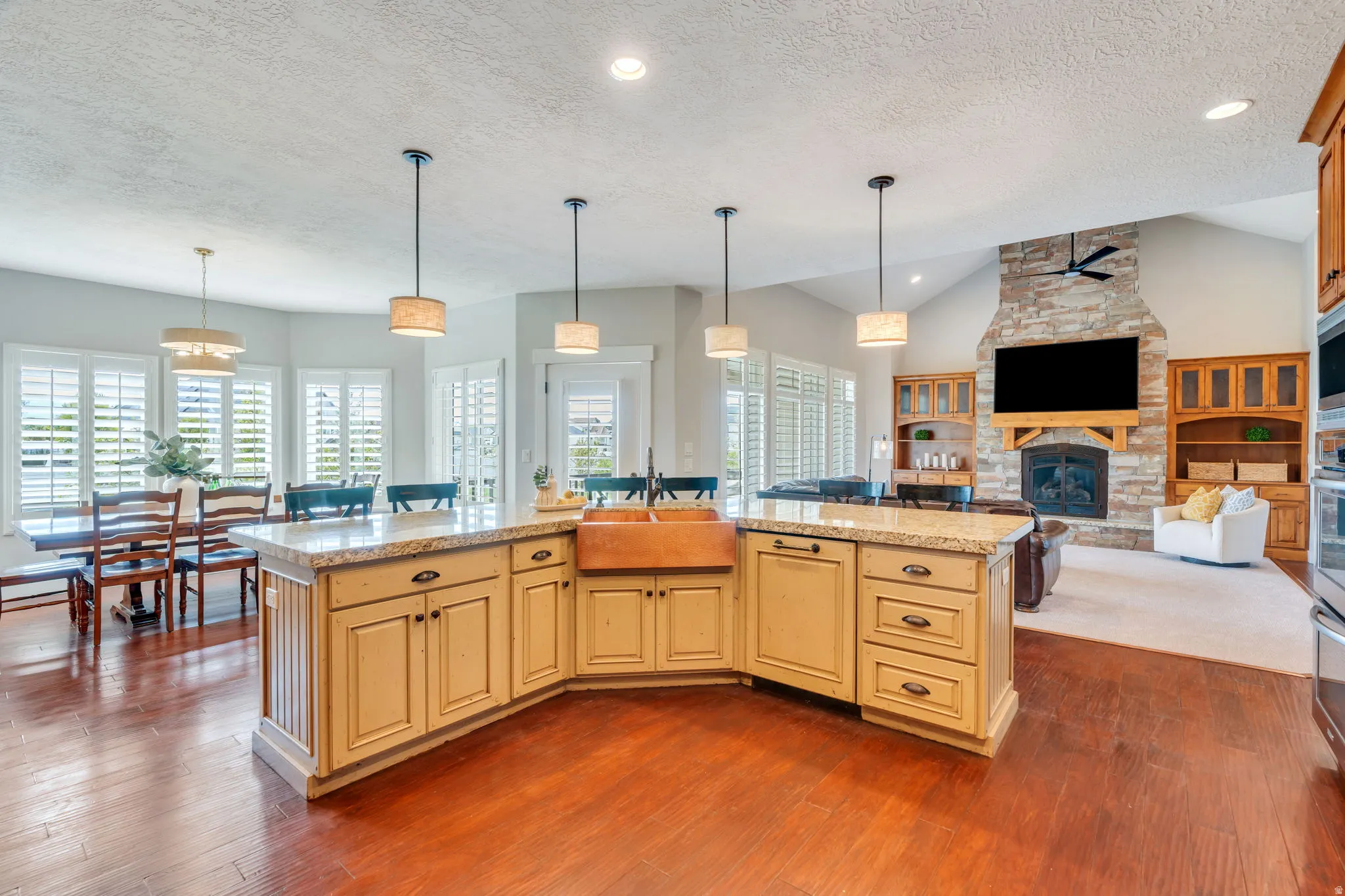 Kitchen with open floor plan, pendant lighting, a fireplace, an island with sink, and light stone countertops