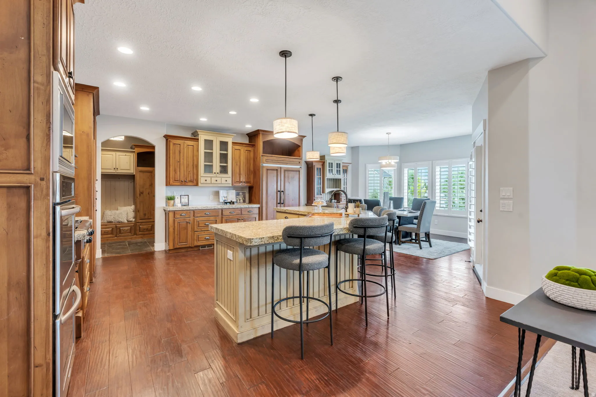 Spacious kitchen featuring wood-finish flooring, two large islands with granite countertops, recessed lighting, and pendant light fixtures
