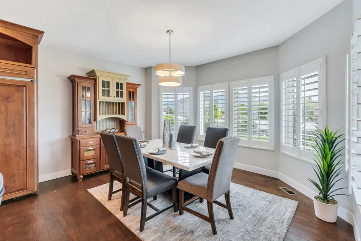 Dining area featuring wood-finish flooring, a contemporary chandelier, and a bay window with plantation shutters