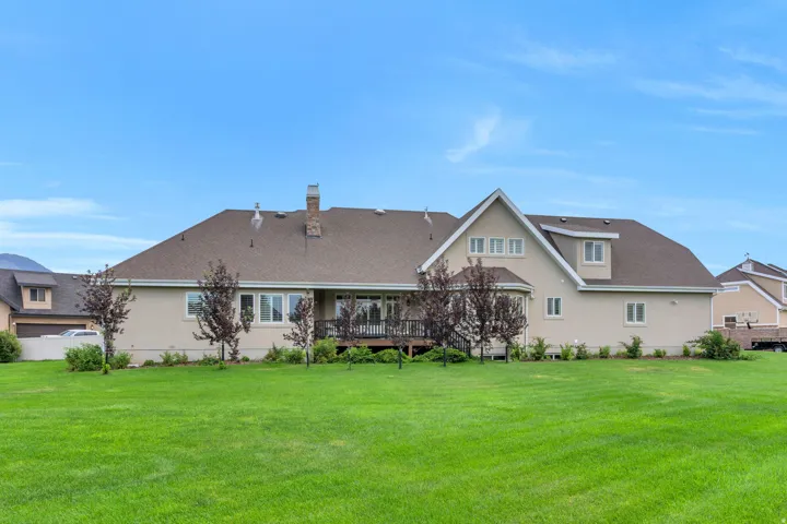 Expansive rear yard featuring a manicured lawn, mature trees, and a spacious deck