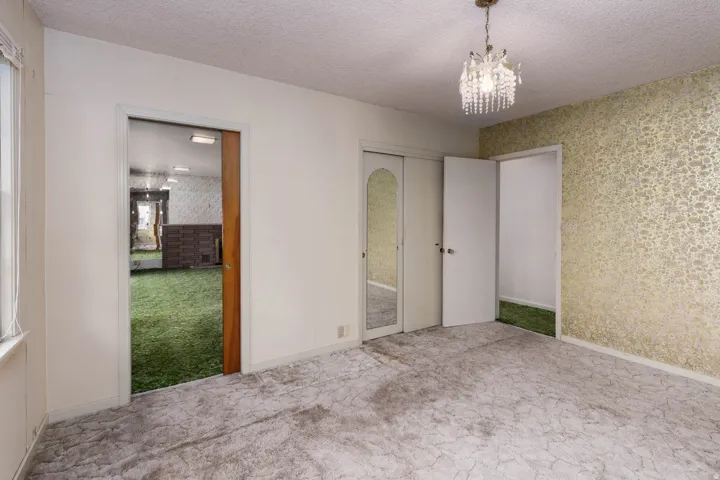 Unfurnished bedroom with wallpapered walls, carpet flooring, a textured ceiling, hanging lights, and ensuite bath