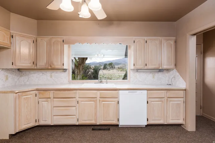 Kitchen with a ceiling fan, dishwasher, light wood finish cabinetry, dark colored carpet, and tasteful backsplash