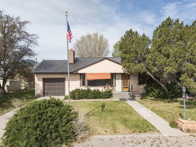 View of front of property with an attached garage, a front lawn, a metal roof, a chimney, and covered porch