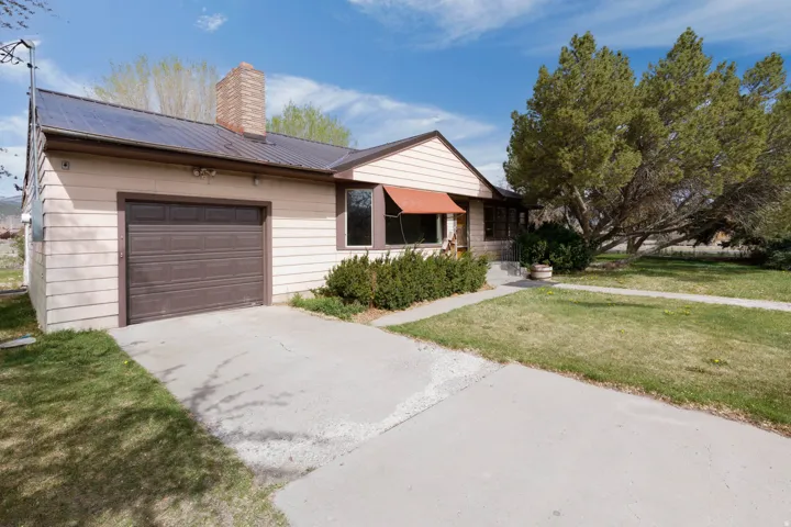 Ranch-style home with a front yard, an attached garage, driveway, a metal roof, and a chimney